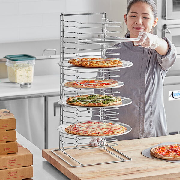 A woman's hand places a pizza on a Choice pizza pan rack.