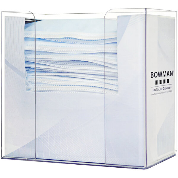 A clear Bowman dispenser holding a box of white earloop face masks.