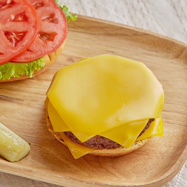 A cheeseburger with Follow Your Heart vegan cheddar cheese and pickles on a wooden plate.