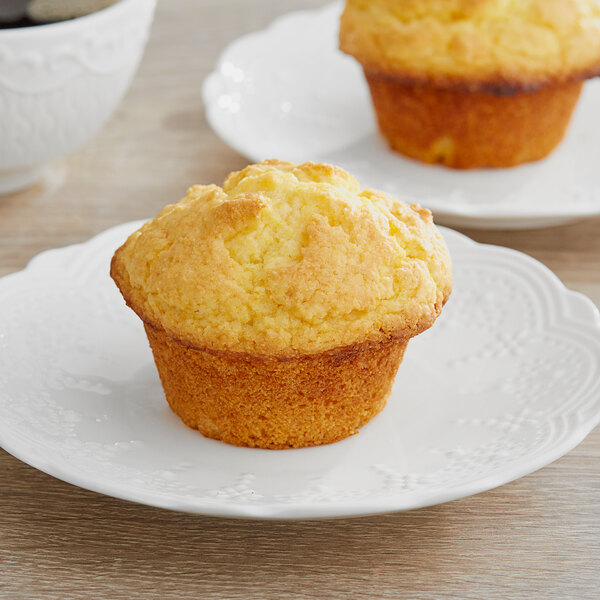 Two corn muffins on white plates with coffee.