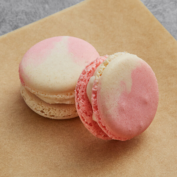 Two white macarons with pink and white frosting on a brown surface.