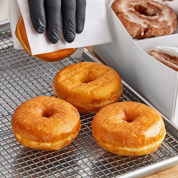 A gloved hand putting a donut in a paper bag.