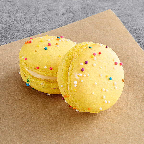 Two yellow macarons with sprinkles on top.