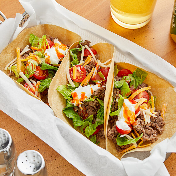 Three tacos with meat and vegetables on a wooden tray.