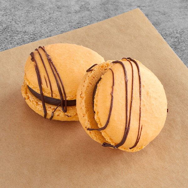 Two Macaron Centrale macarons with chocolate and caramel on brown paper.