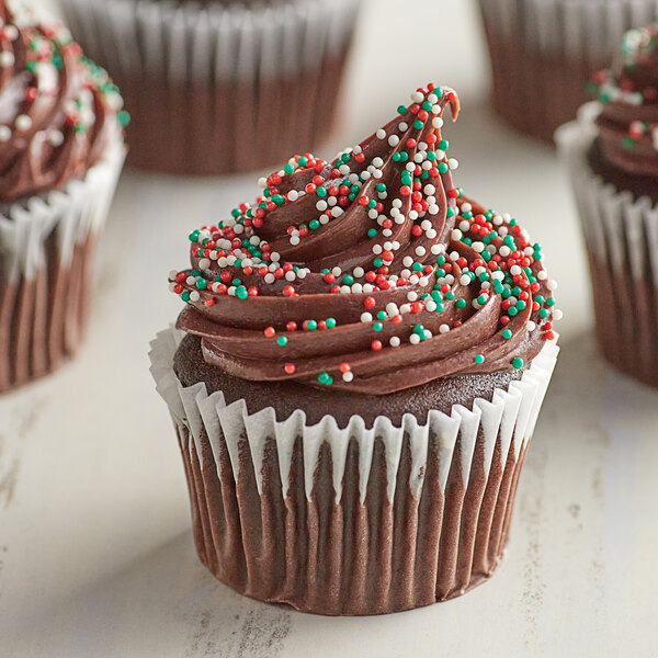A chocolate cupcake with white frosting and Christmas Nonpareil sprinkles.