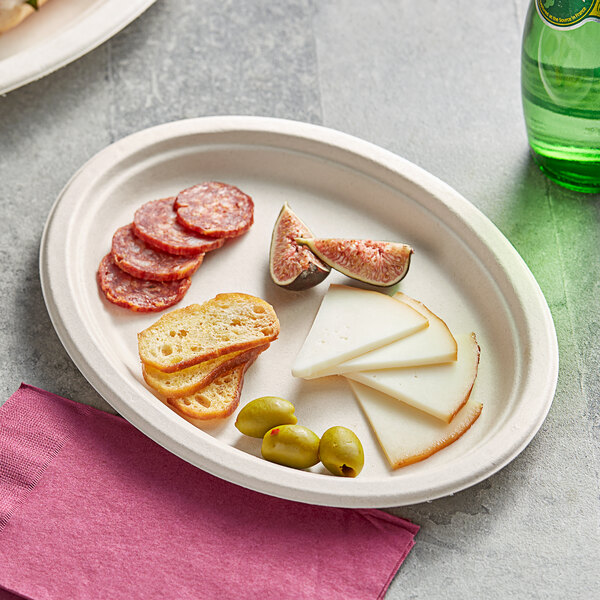 An EcoChoice natural bagasse oval plate with cheese, olives, and bread on it.