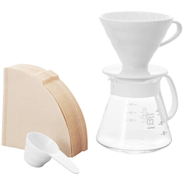 A white Hario coffee dripper, clear glass server, and white measuring spoon.