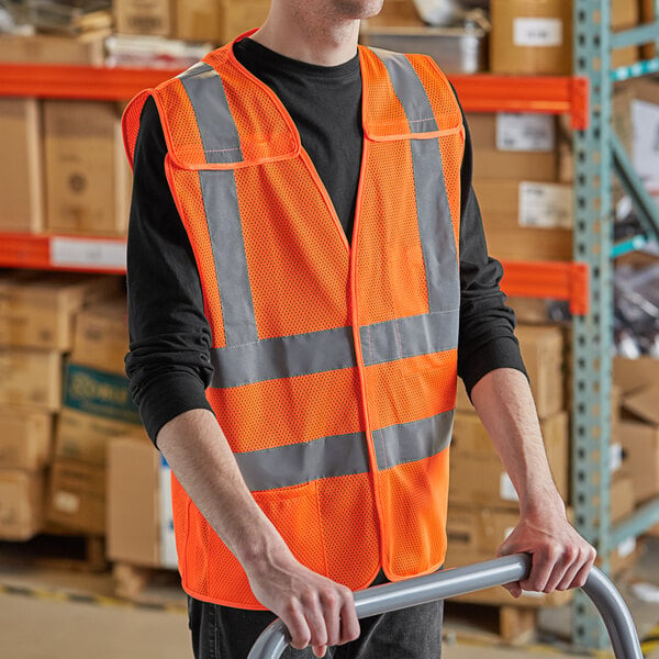 A man in a Lavex orange high visibility safety vest holding a handrail in a warehouse.