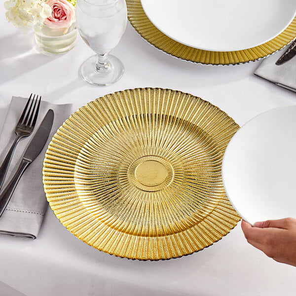 A person holding an Acopa round glass charger plate with a gold sunburst rim.