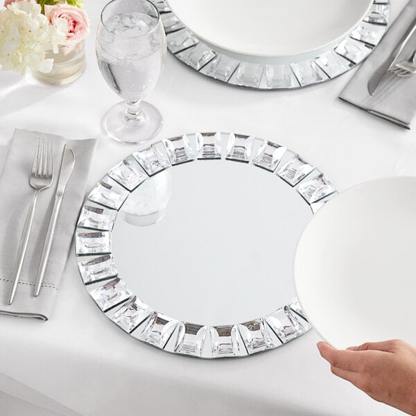 A white table set with a white Acopa jeweled mirror charger plate and silverware.