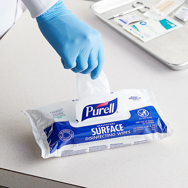 A hand in blue gloves taking a Purell disinfecting wipe from a package.