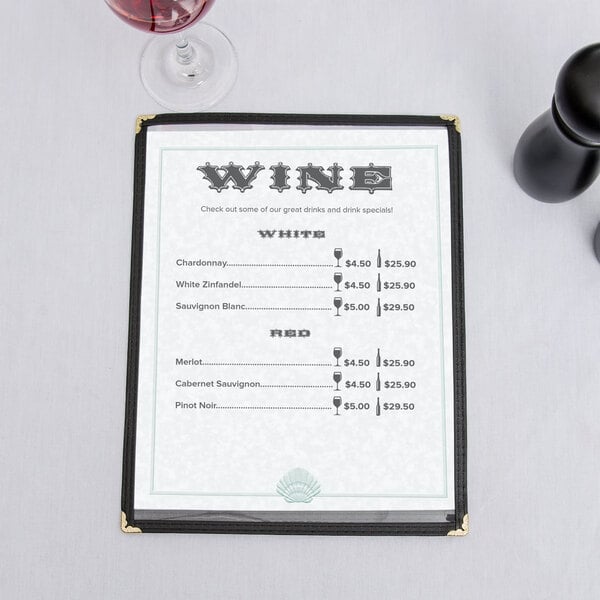 A green menu with a shell border on a table with a glass of wine.