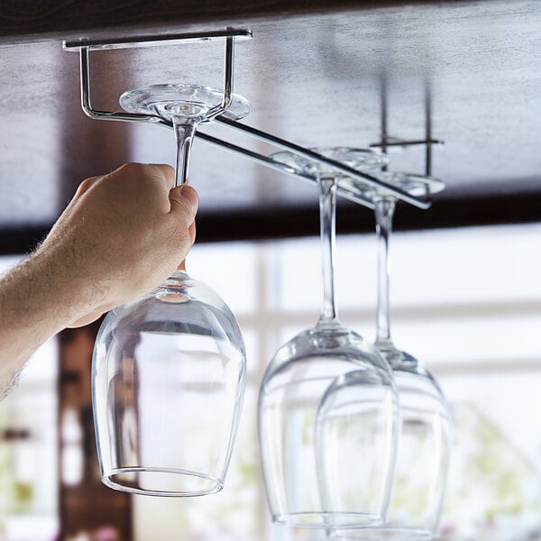 A hand using a Regency chrome plated glass hanger rack to hang wine glasses over a counter.