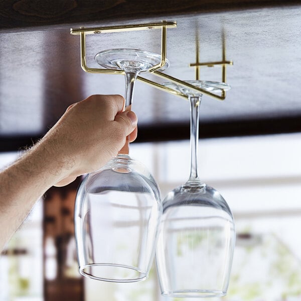 A hand using a Regency brass plated glass hanger to hold two wine glasses over a table.