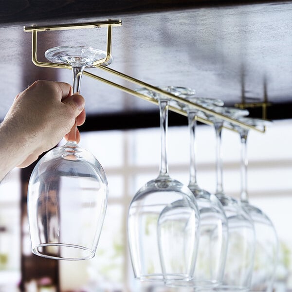 A hand holding a wine glass over a Regency brass plated glass hanger rack.