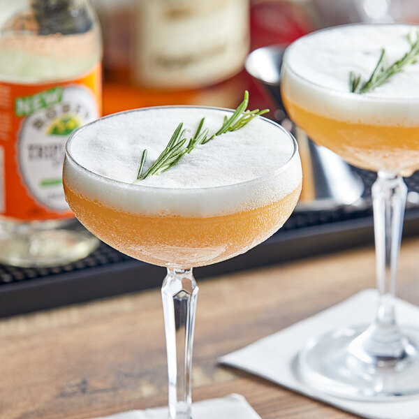 Two glasses of Rose's Triple Sec on a table with a sprig of rosemary garnish.