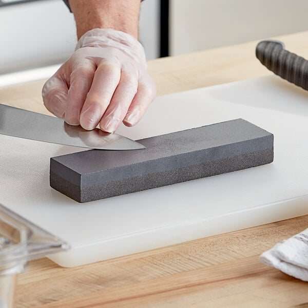 A hand holding a Choice carbonized silicon knife sharpening stone and a knife.