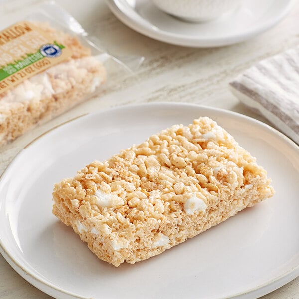 A rectangular white Sweet Street Gluten-Free Chewy Marshmallow Bar on a plate next to a plastic bag of food.