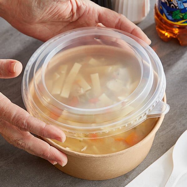 A person's hand holding a Choice polypropylene take-out lid over a bowl of soup.