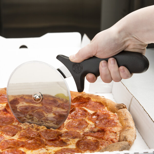 A person using an American Metalcraft stainless steel pizza cutter with a black handle to cut a pizza.