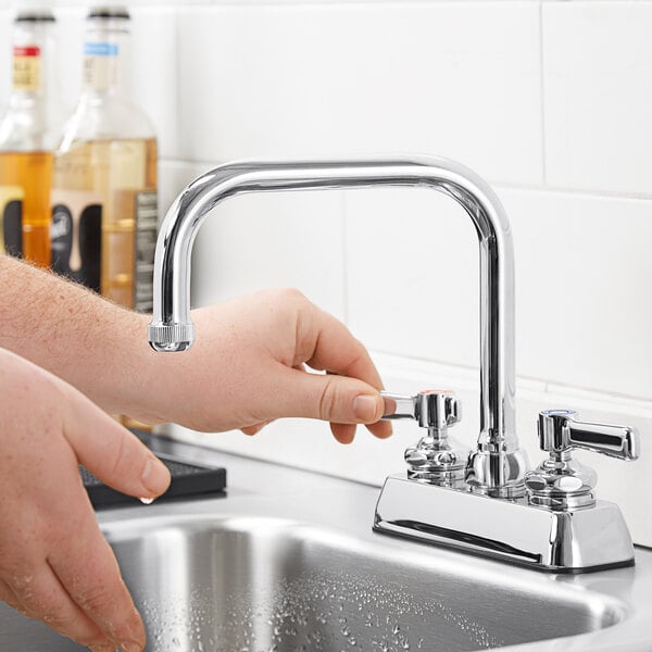 A person's hand turning a Chicago Faucets deck-mounted faucet on a counter.