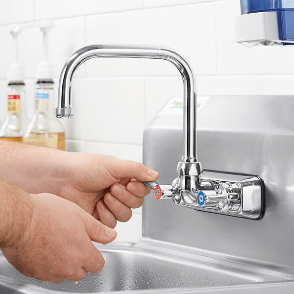 A person's hands turning a Chicago Faucets wall-mounted sink faucet.
