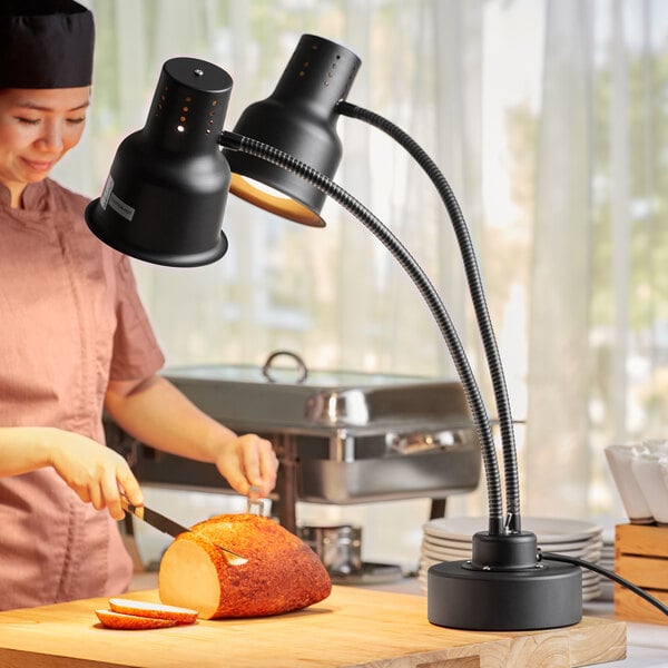 A woman in a chef's hat using an Avantco dual arm heat lamp to cut a piece of bread.