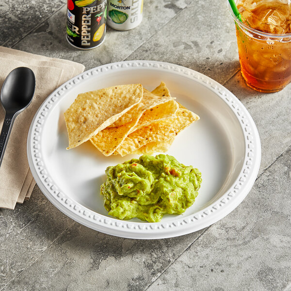 A Huhtamaki Chinet white plastic plate of tortilla chips and guacamole on a table.