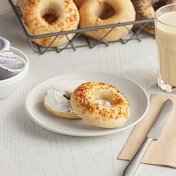 A plate with a Greater Knead Gluten-Free Onion Bagel next to a basket of bagels and a glass of milk.