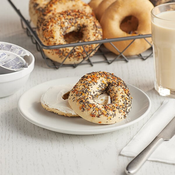 A Greater Knead gluten-free everything bagel with black and orange sprinkles on a plate with other bagels and a glass of milk.