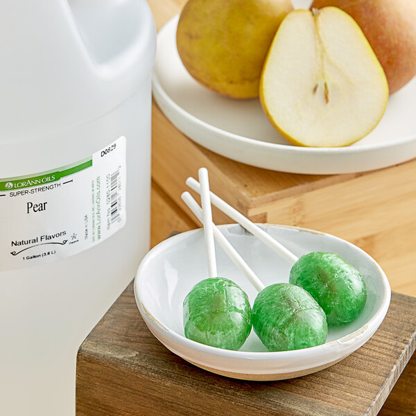 A bowl of lollipops next to a container of LorAnn Oils Pear Super Strength Flavor.