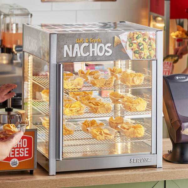 A woman serving nachos from a ServIt countertop food display case.