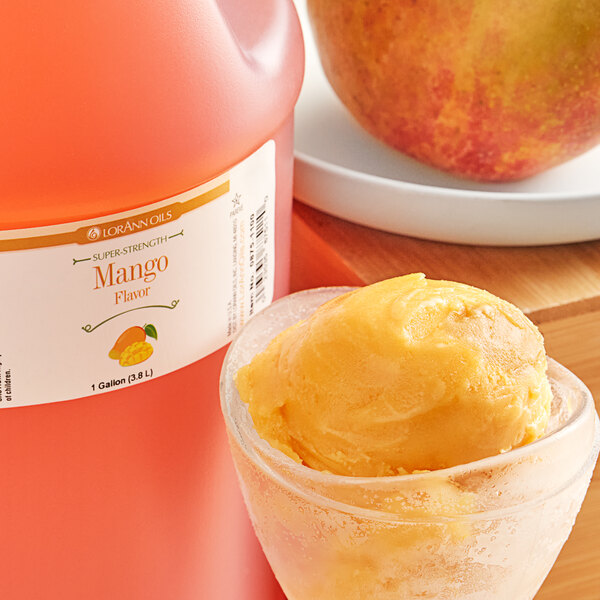 A cup of yellow mango ice cream on a table with a bottle of LorAnn Oils Mango Super Strength Flavor.