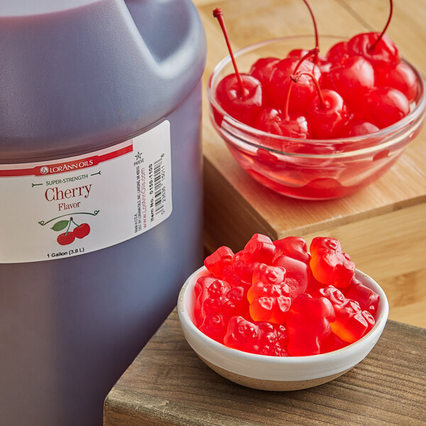 A jug of LorAnn Oils Cherry Super Strength Flavor on a counter with a bowl of gummy bears.