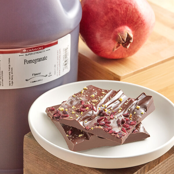 A plate of chocolate with nuts and seeds on it next to a LorAnn Oils Pomegranate Super Strength Flavor bottle and a chocolate bar.