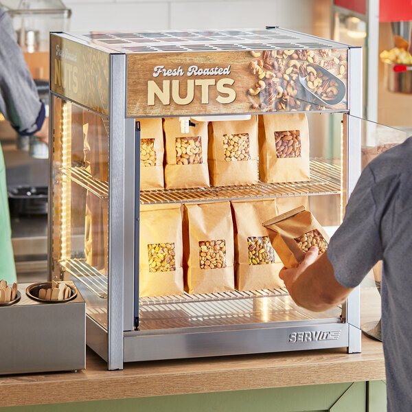 A man standing at a ServIt countertop display case filled with bags of peanuts.