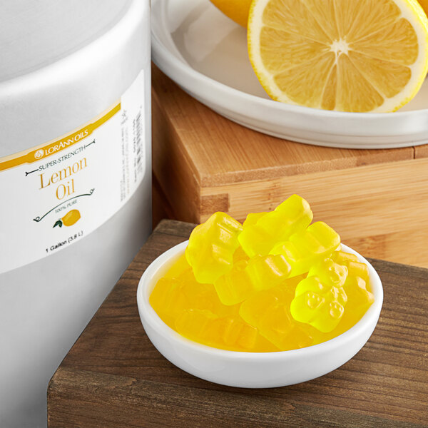 A bottle of LorAnn Oils All-Natural Lemon Super Strength Flavor on a counter next to lemons.