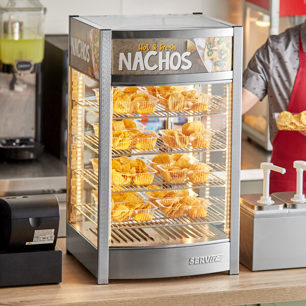 A man using a ServIt countertop nacho warmer to display trays of potato chips.