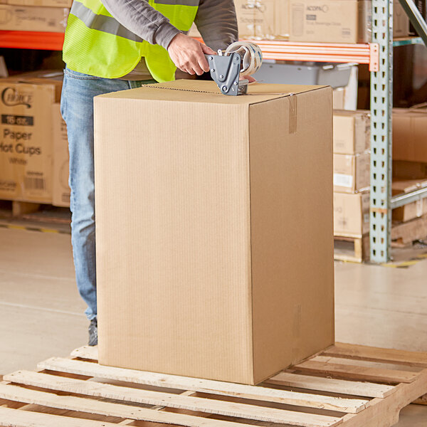 A man in a yellow vest and jeans standing on a pallet with a Lavex cardboard shipping box.