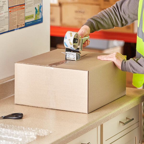 A person using a machine to seal a Lavex cardboard shipping box.