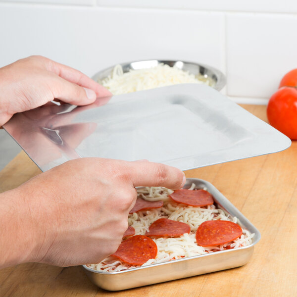 A person putting a plastic cover over a square pizza.