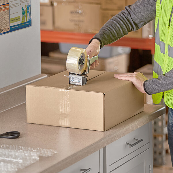 A person in a safety vest using a tape gun to seal a Lavex shipping box.