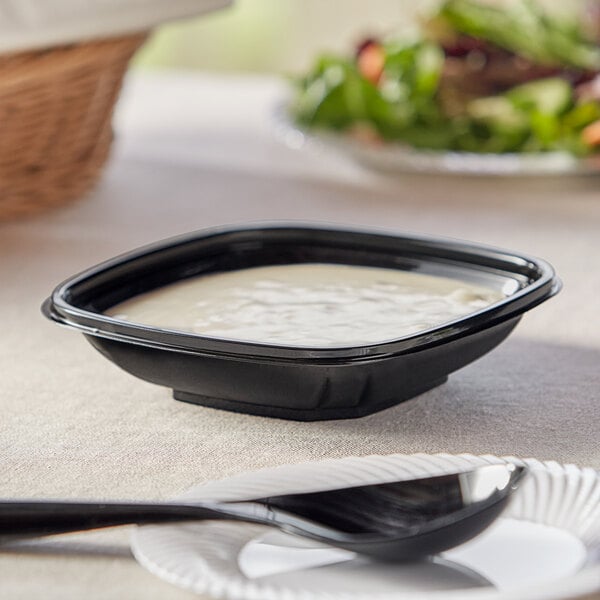 A Visions black plastic square bowl filled with white sauce on a table.