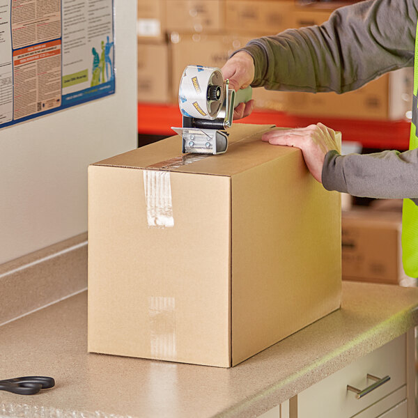 A person using a tape dispenser on a Lavex shipping box.