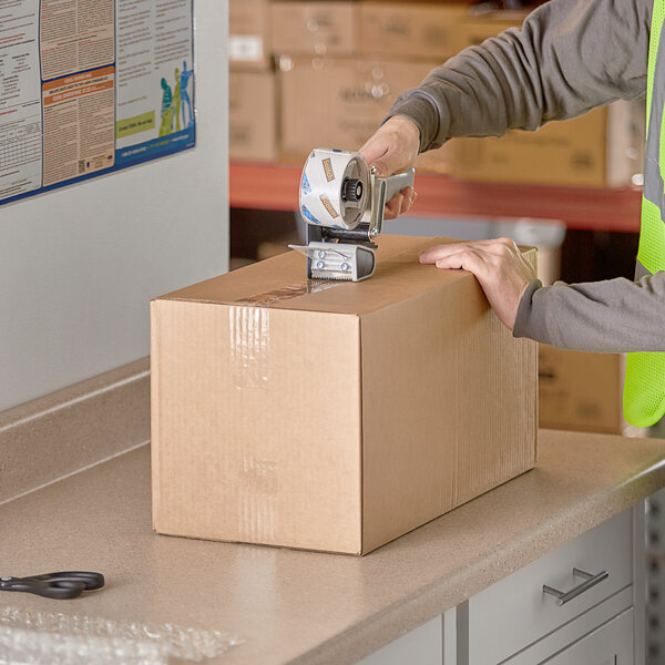 A person using a tape gun to seal a Lavex Kraft shipping box.