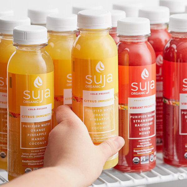 A hand holding a red case of Suja Citrus Immunity Cold-Pressed Juice bottles.