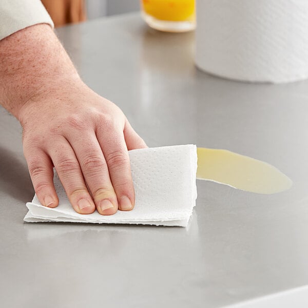 A hand holding a Tork Universal paper towel over a counter.