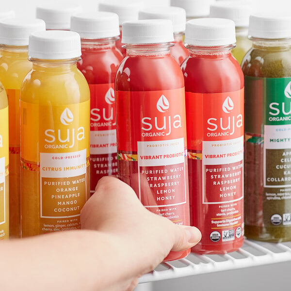 A hand holding a bottle of Suja Vibrant Probiotic Juice with a green and white label.