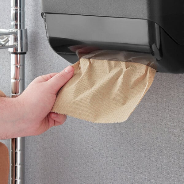 A hand using Tork Natural Kraft singlefold paper towels to clean a surface.
